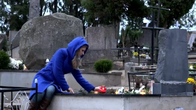 女人坐在坟墓上母亲祖母放蜡烛祈祷。