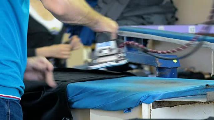 特写一名工人在纺织品生产上熨烫衣服