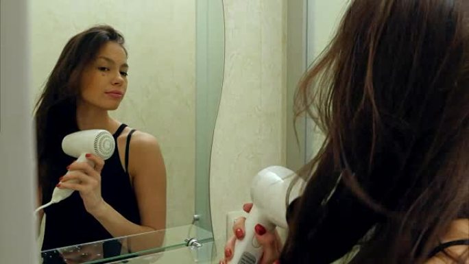 年轻迷人的女孩在酒店浴室用吹风机吹干头发