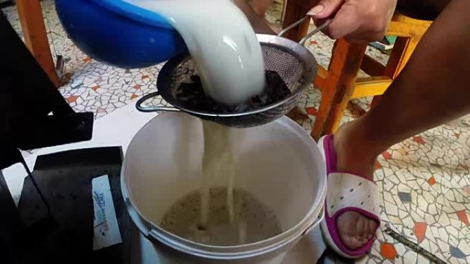 茶和牛奶通过一个筛子倒入白桶，一个女人的脚