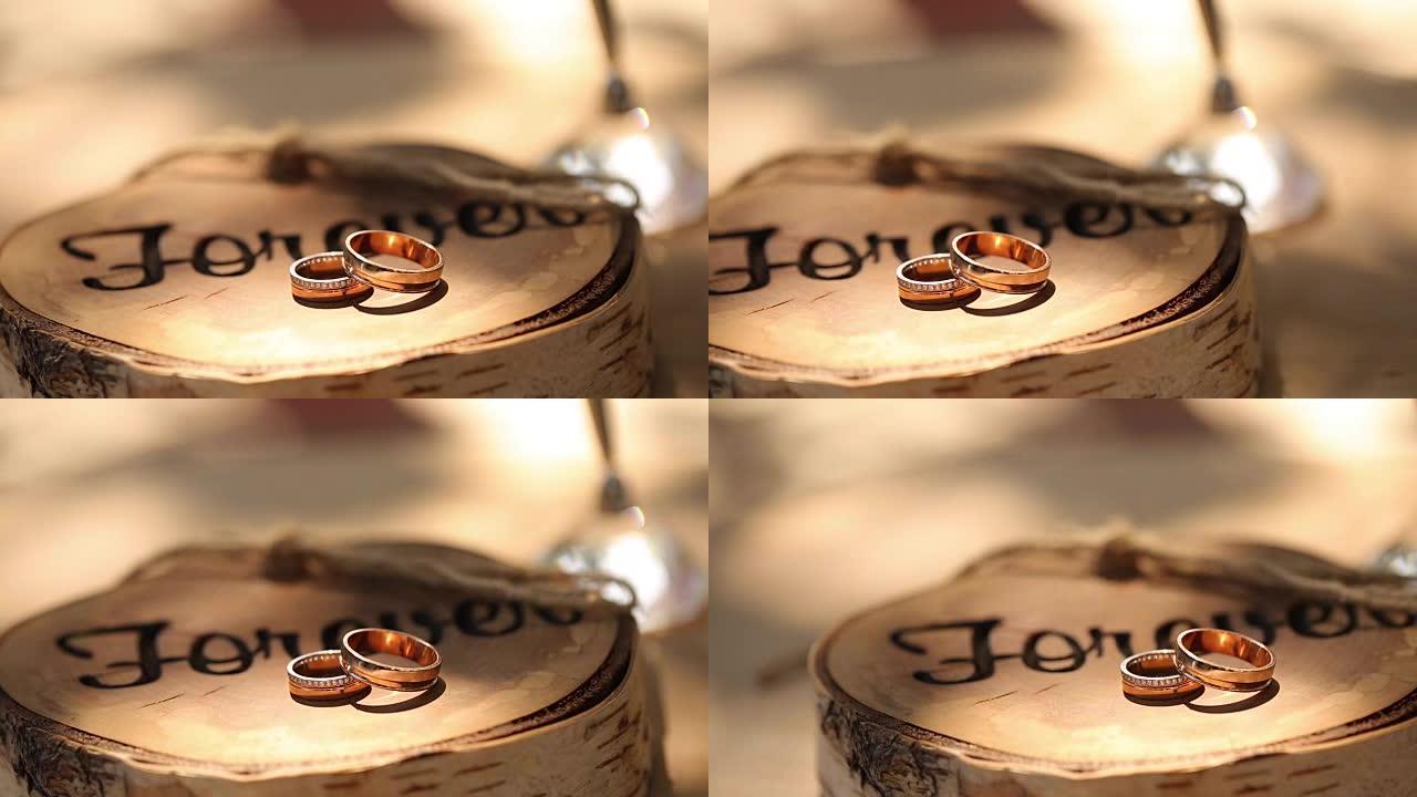 结婚戒指躺在树桩上的木制乡村风格的架子上，在新郎和新娘的仪式上刻有 “永远” 字样