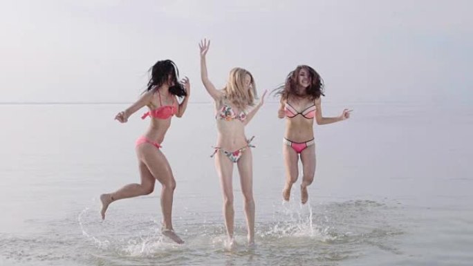 三个十几岁的女孩在海滩日落时在水中跳舞。慢动作