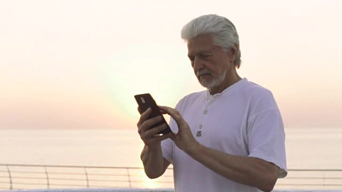英俊的高级男子在海边户外使用智能手机，背景为海洋
