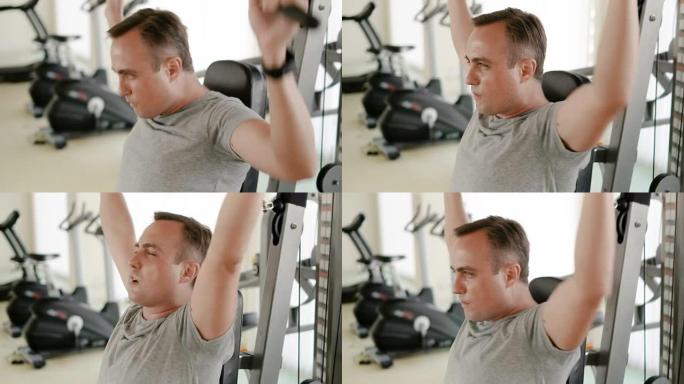 穿着灰色t恤的坚定健身运动年轻人在健身房举重机器上锻炼