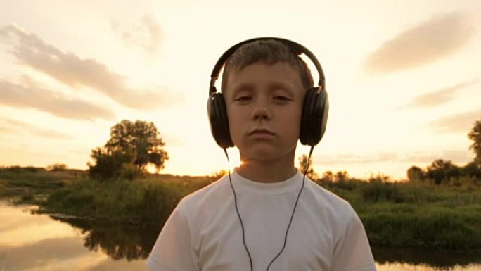 男孩在夕阳下的大自然中通过耳机听音乐