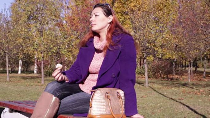 吃冰淇淋的女人坐在秋园的长凳上