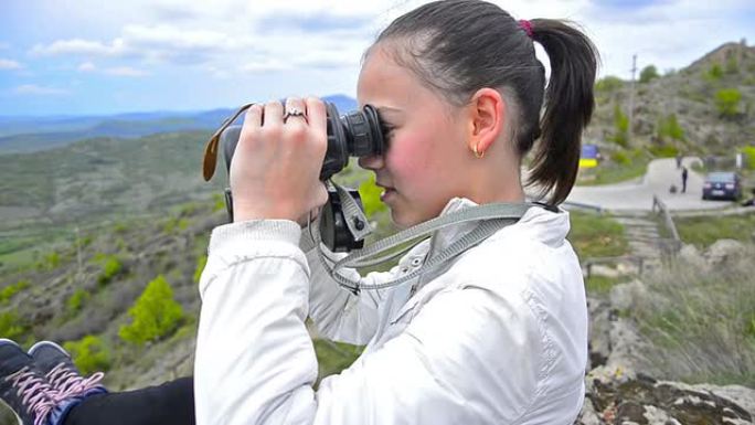 年轻女孩用双筒望远镜在山顶徒步旅行