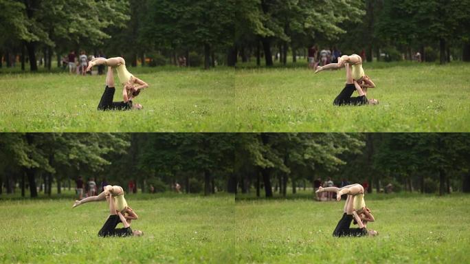 练习acro瑜伽的美丽夫妇。年轻的瑜伽教练在绿色草地上的城市公园练习。两个成功的年轻人进行acro瑜