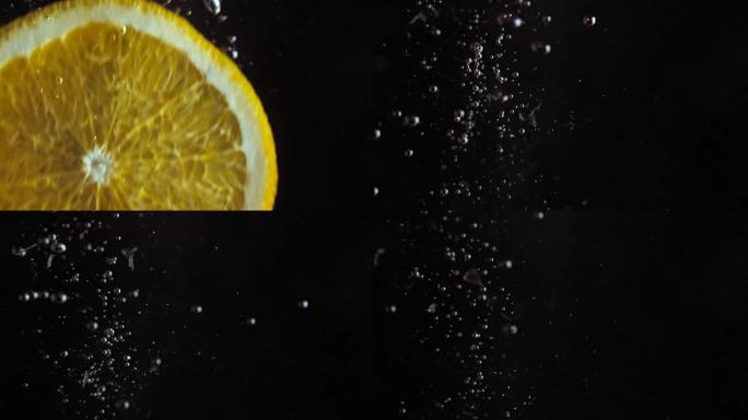 超级特写镜头。宏观观。切成薄片的多汁新鲜橙子以慢动作落入水中。黑色背景上的气泡