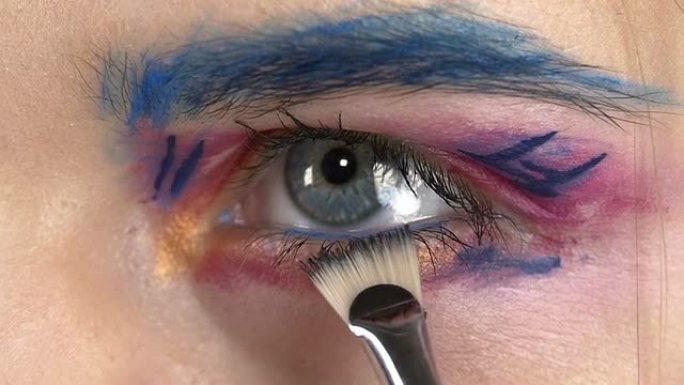 眼底彩妆女人涂抹眼影，制作异国情调，一个，蓝色眉毛，黄色阴影，睫毛膏，用特殊刷子画龙点睛，特写，白色