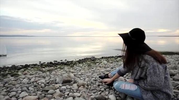 坐在圆石滩上的年轻女子向水中投掷石块