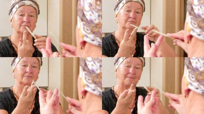 年纪大的女人在浴缸里自己修指甲。它使用指甲锉。可以看到它在镜盒中反射。美容概念