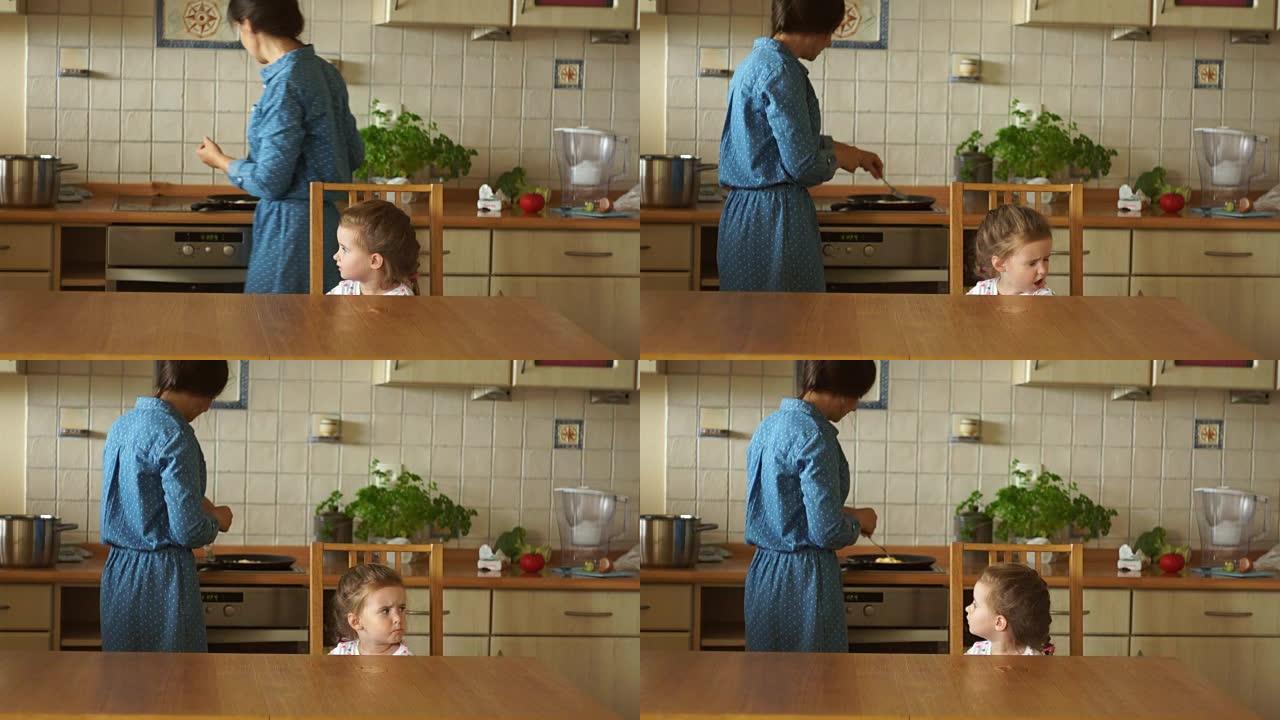 妈妈在炉子上煮鸡蛋。一个小女儿在餐桌旁等着吃早餐。这个女孩很生气。幼稚的异想天开。家庭早餐。
