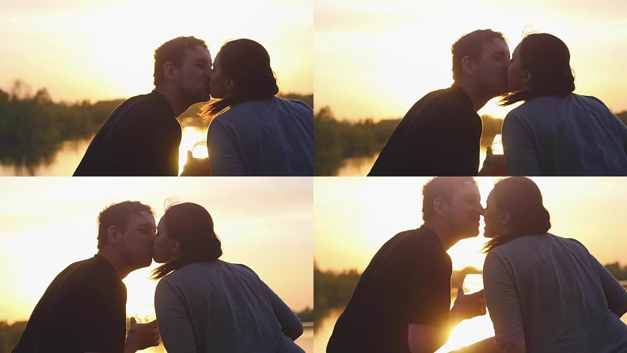 恋爱中的年轻夫妇在日落时在海边亲吻和喝酒。他们坐在沙滩上，以慢动作碰杯。周年纪念或蜜月。1920x1