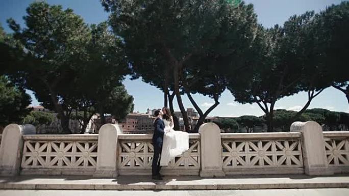 意大利罗马浪漫石桥上的婚礼情侣。时尚的新郎与美丽的新娘接吻。意大利、欧洲的蜜月