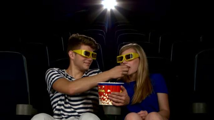 伟大的电影!年轻夫妇在电影院互相喂食。3D眼镜