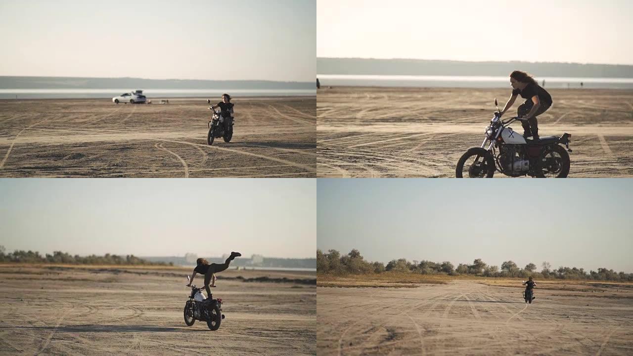 美丽的年轻女子骑着摩托车骑在一辆旧摩托车上，做了一个把戏。日落或日出时在沙漠中。女自行车手。慢动作