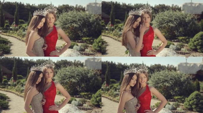 两个性感的年轻女性在美丽的花园里穿着晚礼服和皇冠摆姿势