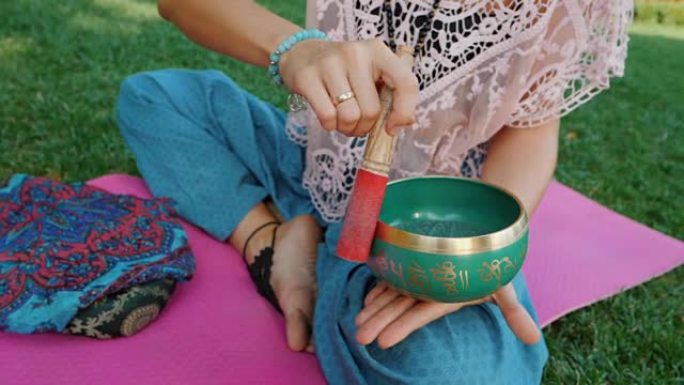 夏天，女人坐在公园的粉红色瑜伽垫上玩唱歌碗。复古tonned。美丽的女孩，带着马拉珠在绿草上冥想。慢