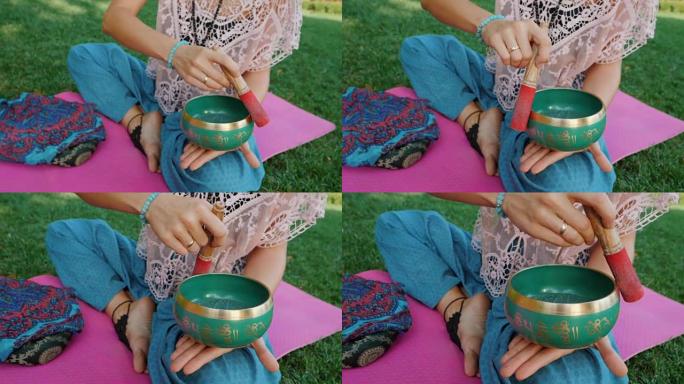 夏天，女人坐在公园的粉红色瑜伽垫上玩唱歌碗。复古tonned。美丽的女孩，带着马拉珠在绿草上冥想。慢