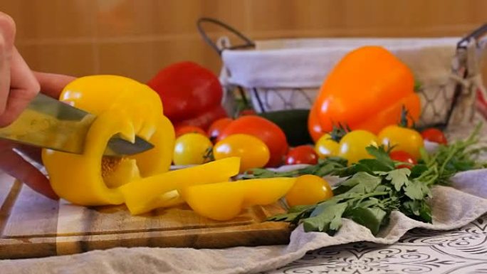 女人在厨房做饭。将黄胡椒倒入小方块中。桌子上有很多不同的蔬菜。多汁成熟的西红柿和黄瓜