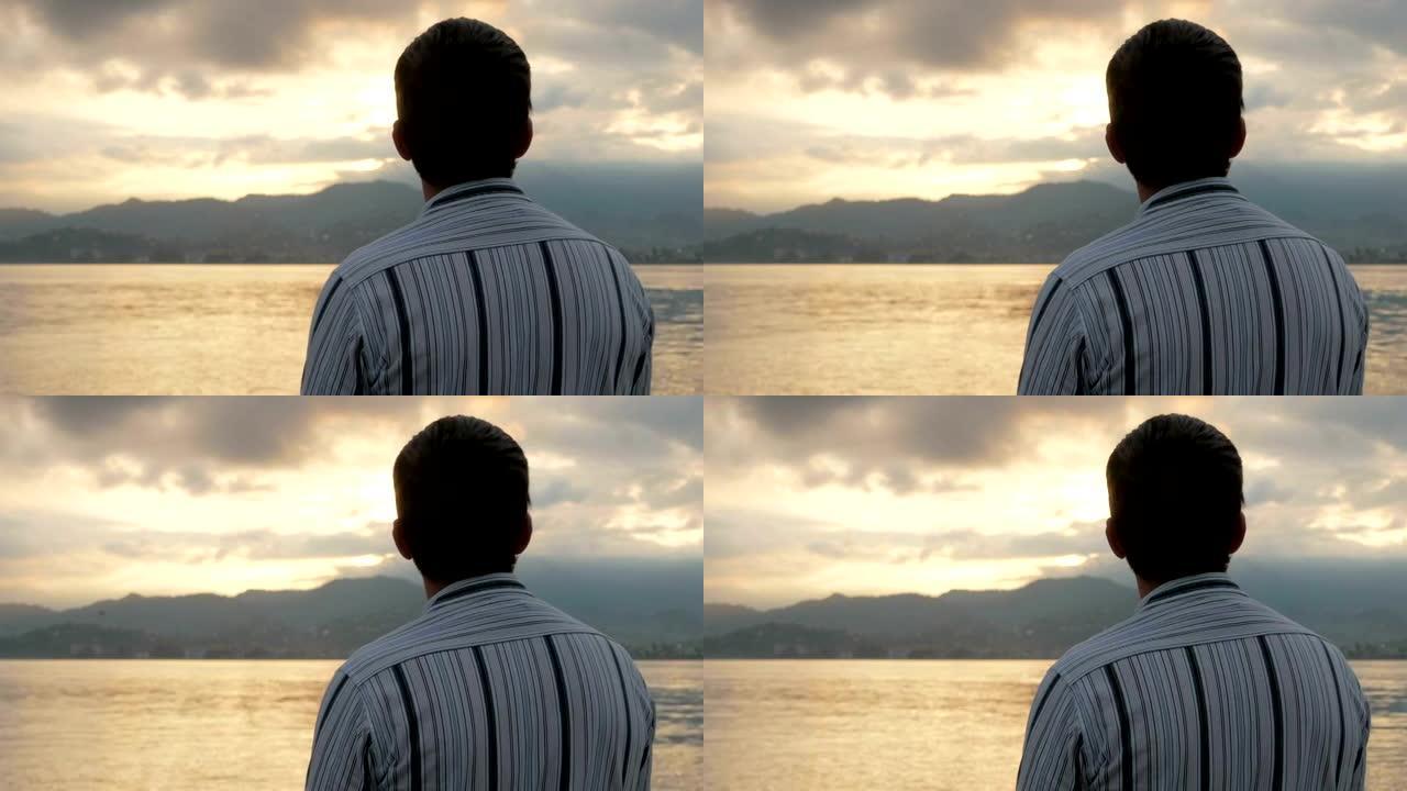 这个男人穿着衬衫看着海边的日出。太阳从山后升起。自然崇拜的概念