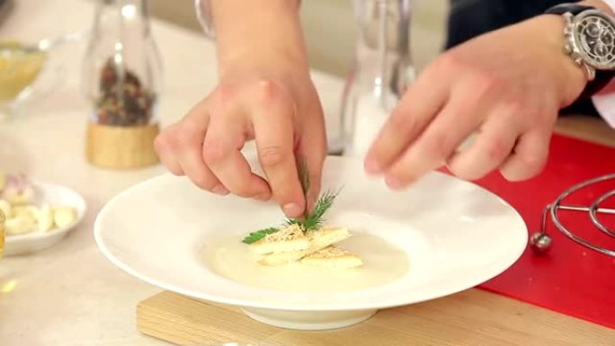厨师正在将莳萝，欧芹，盐和胡椒粉放在盘子里，上面放着奶油汤，酥脆的吐司和磨碎的奶酪