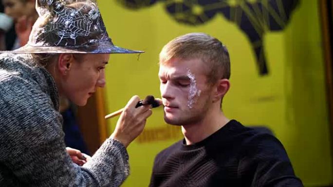 万圣节派对，化妆师为万圣节派对在一个男人的脸上画了一个可怕的妆容。在背景中，可以看到万圣节风格的风景
