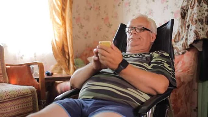 老人拿着电话坐在家里的皮椅上。男子打短信看照片