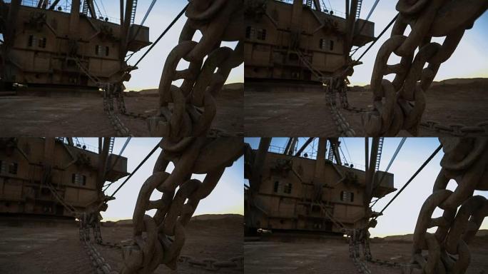 手持拍摄拖曳挖掘机巨大的斗链站在采石场边，落日映衬下的蓝天。