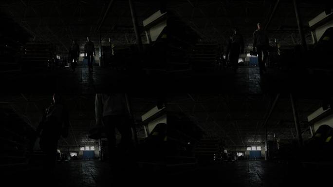 两个年轻人带着工具在黑暗的机库里对着摄像机
