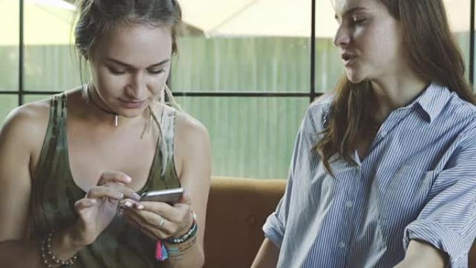 两个年轻的女友使用智能手机并在咖啡馆聊天