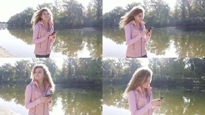 女人用智能手机短信聊天户外散步河边，卷发女孩早秋公园自然阳光