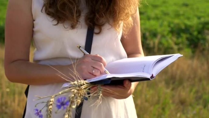 女手用笔在外面草地上的笔记本上写字