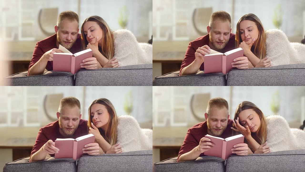 年轻可爱的夫妇躺在沙发上看书
