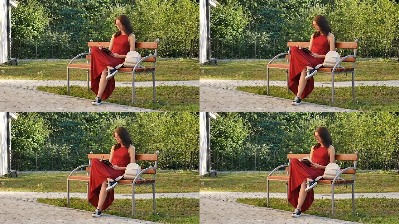戴着眼镜和红色长裙的聪明女学生坐在公园的长凳上，在笔记本上写东西。