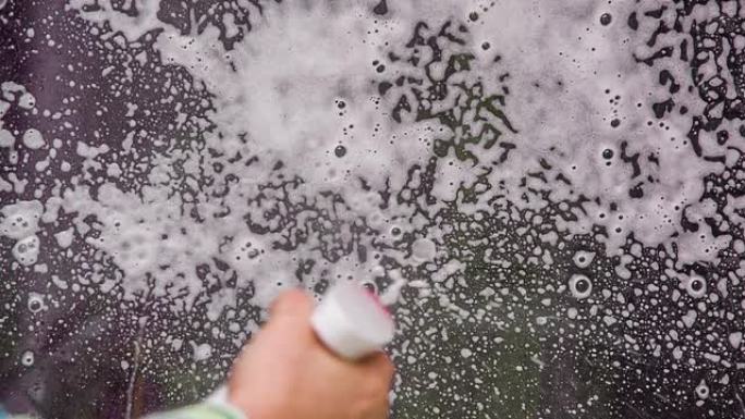 人的手在房子的窗户上喷涂洗涤泡沫