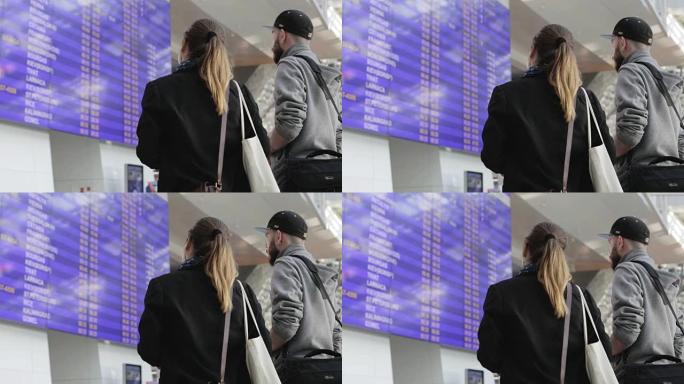 年轻的游客夫妇在机场看航班时刻表。
