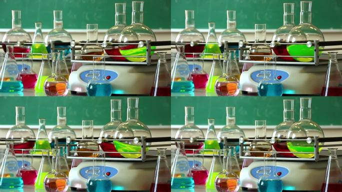 带有彩色液体的实验室玻璃器皿在两个振动台上旋转，一些烧瓶围绕另一个纵横角度站立