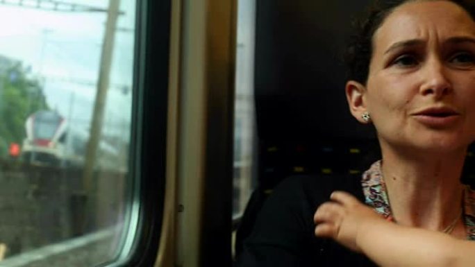在火车上随意偷拍母亲和婴儿的照片。妈妈在通勤时亲吻疲惫的婴儿。婴儿想睡觉