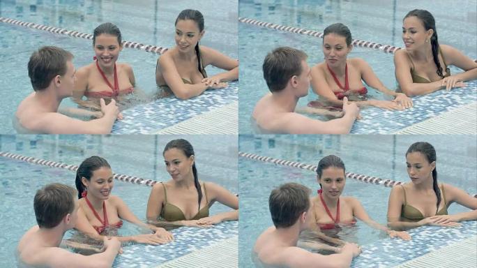 两个漂亮的女人在游泳池里和一个年轻人说话