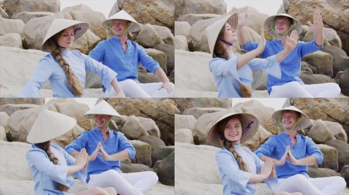 一个戴着越南帽子的男孩和一个女孩以瑜伽姿势坐在海滩上的岩石上，冥想并互相看着对方。蜜月约会和幸福家庭