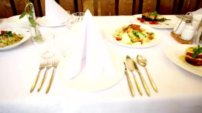 宴会桌，桌上有美餐的菜肴，叉子眼镜，刀，餐具躺在盘子附近，肉，沙拉，桌子上有很多食物