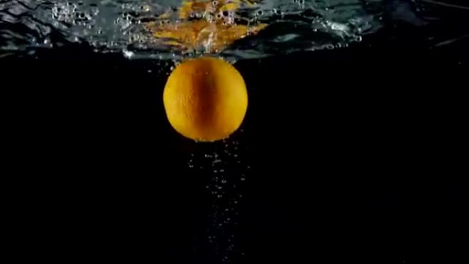 黑色背景上飞溅的新鲜水果橙色掉入水中