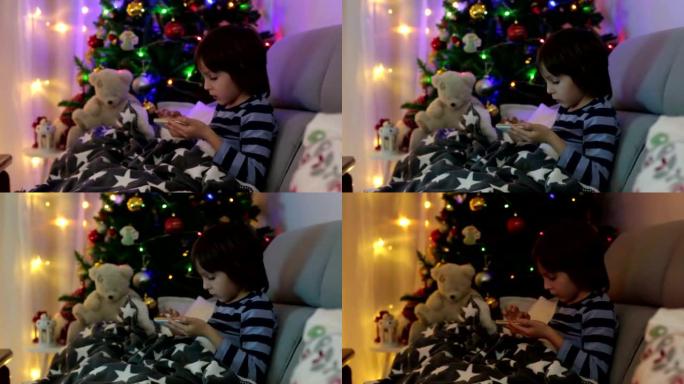可爱的可爱的孩子，男孩，在第一个降临节星期天在毯子下玩手机，在他们身后的圣诞树