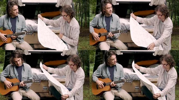 男子在露营时看着纸质地图，而他的男性朋友在弹吉他