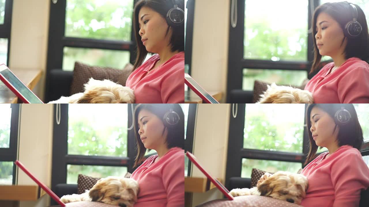 海: 使用手机，轻松的女人戴着耳机在咖啡馆里与狗一起在数字平板电脑上听音乐。