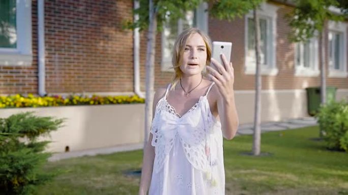 穿着白色蕾丝连衣裙的年轻迷人女子去散步，在视频聊天中与她的朋友交谈
