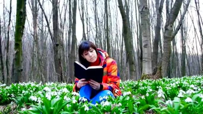 一个美丽的聪明女孩正在充满雪花的春天森林里读一本有趣的书