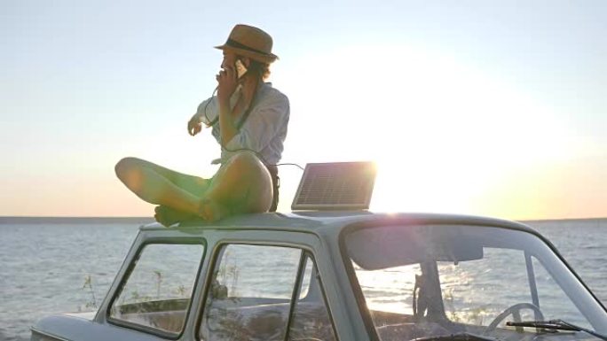 生态旅游，女孩坐在背光的车顶上，用手机聊天，拿着太阳能电池，年轻女子使用太阳能电池